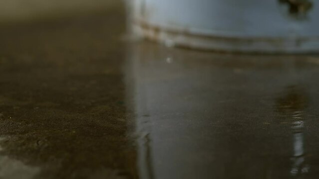 A tilt shot following the water leak to the pressure relief valve tube on the side of an electric water heater, which explodes releasing hot water and steam onto the concrete floor of a basement