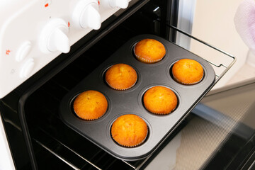 Caucasain woman holding tray with freshly made cupcakes or maffins at the kitchen
