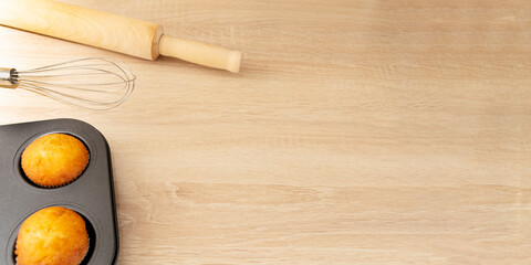 tray with freshly made cupcakes or muffins on wood background with cooking tools