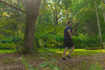 A man athlete runs in the park outdoors, around the forest, oak trees green grass young enduring athletic athlete athlete forest, lifestyle outdoor athletic legs motion, outside. Summer running