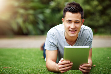 Online no matter where I am. Portrait of a handsome young man using a digital tablet while lying on the grass outside.