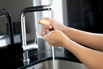Hands of woman wash their hands in a sink with foam to wash the skin and water flows through the hands. Concept of health, cleaning and preventing germs and coronavirus from contacting hands