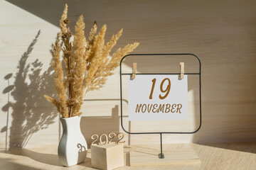 november 19. 19th day of month, calendar date. White vase with dead wood next to the numbers 2022 and stand with an empty sheet of paper on table. Concept of day of year, time planner, autumn month