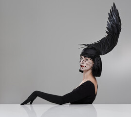 Just winging it. Shot of a young woman in a wing-shaped headpiece sitting in a studio.