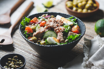 Canned tuna salad with fresh vegetables, capers and olives in a black bowl. Healthy lunch or dinner.