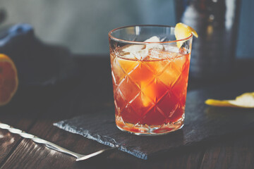 Orange or red coctail in an old fahion glass with citrus and ice cubes on a bartender table. Mixology concept.