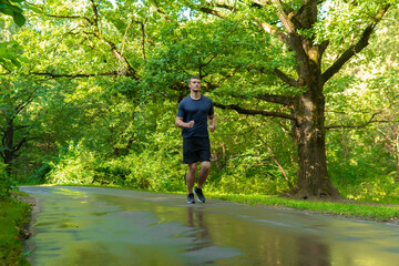 A man athlete runs in the park outdoors, around the forest, oak trees green grass young enduring athletic athlete run sport forest, lifestyle athletic jog, jogging outside. Autumn leisure running