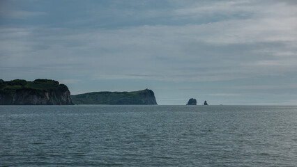 The picturesque coast of Kamchatka against the blue sky. The hills with steep slopes are covered with green vegetation. Ripples on the surface of the Pacific Ocean.