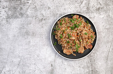 Buckwheat pilaf with meat on a round plate on a dark grey background. Top view, flat lay