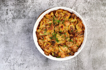 Oven baked potatoes with champignons mushrooms and cheese in a white baking dish on a dark grey background. Top view, flat lay
