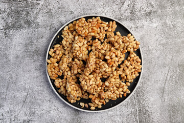 Homemade Peanut brittle  on a round plate on a dark gray background. Top view, flat lay