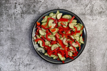 Cucumber and bell pepper salad on a round plate on a dark gray background. Top view, flat lay