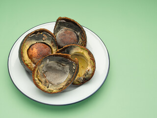 Rotten avocados cut in half on a white plate over a green background