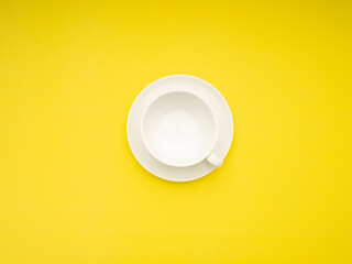 Top view of an empty white ceramic coffee cup on a yellow background