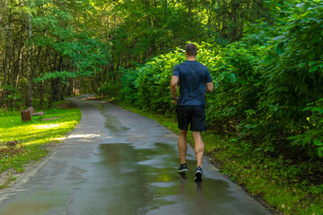 A man athlete runs in the park outdoors, around the forest, oak trees green grass young enduring athletic athlete runner fitness outdoor fit legs male, trees outside. Summer body feet stretches