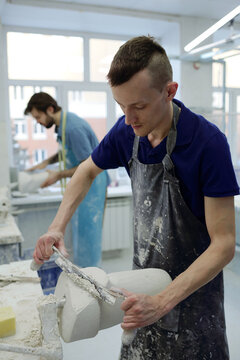 Worker Of Prosthetic Factory Cutting Upper Part Of Plaster Cast While Forming Shape Of Residual Limb Against Colleague