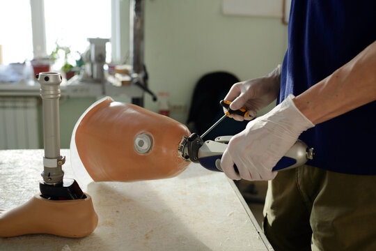Gloved hands of manual worker fixing mechanism of new artificial limb with screwdriver while assembling leg prosthesis