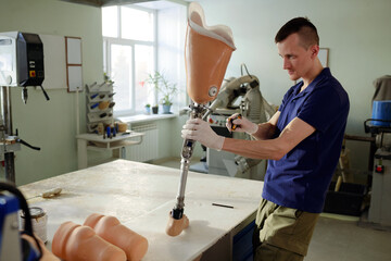 Worker of prosthetic production factory fixing socket covered with silicone liner of leg prosthesis with screwdriver in workshop