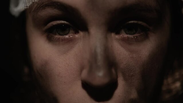 War, accident, crying woman. Close-up of eyes with tears of injured woman with dirty face and bandaged head, she looks sadly and intently into camera. Slow motion
