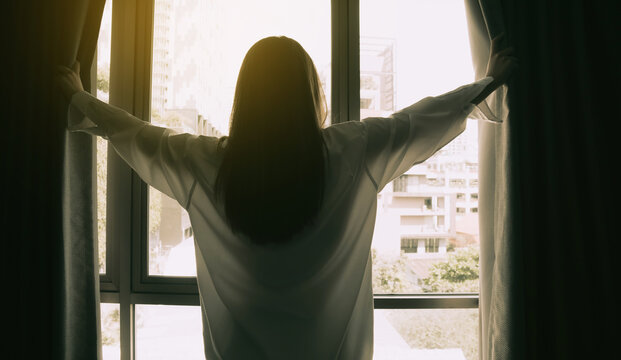 Overjoyed Young Beautiful Woman Standing By Bedroom And Opening Curtains Look In Window Distance Meet Welcome New Day. Smiling Female Feel Excited About Life Career Opportunities Or Perspectives.