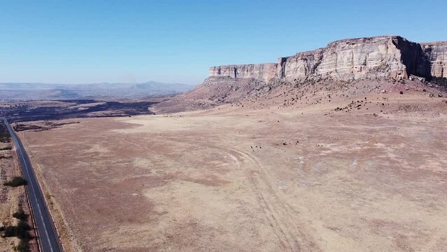Aerial drone shot descending down to a remote rural road which navigates around a spectacular sandstone mountain in the Drakensberg, KwaZulu Natal, South Africa