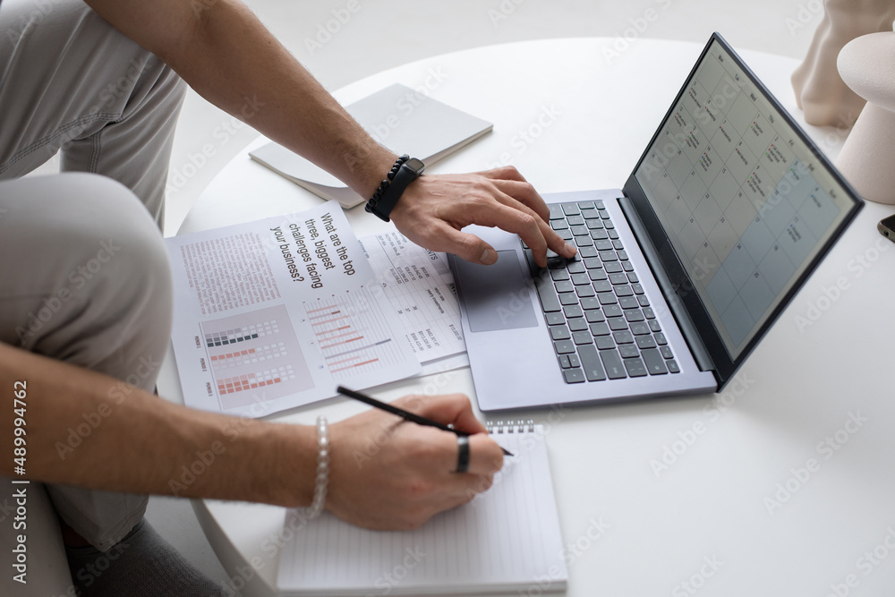 Poster hand of young male auditor or analyst looking through document on laptop screen while pressing one o