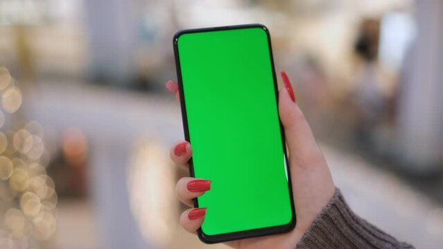 Hands of a young woman holding a smartphone in a shopping mall. A young woman holds a phone in a shopping mall in front of the New Year's decorations. Close-up