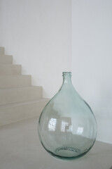 Big drop shaped glass vase standing on the floor of contemporary stylish living room of white color...