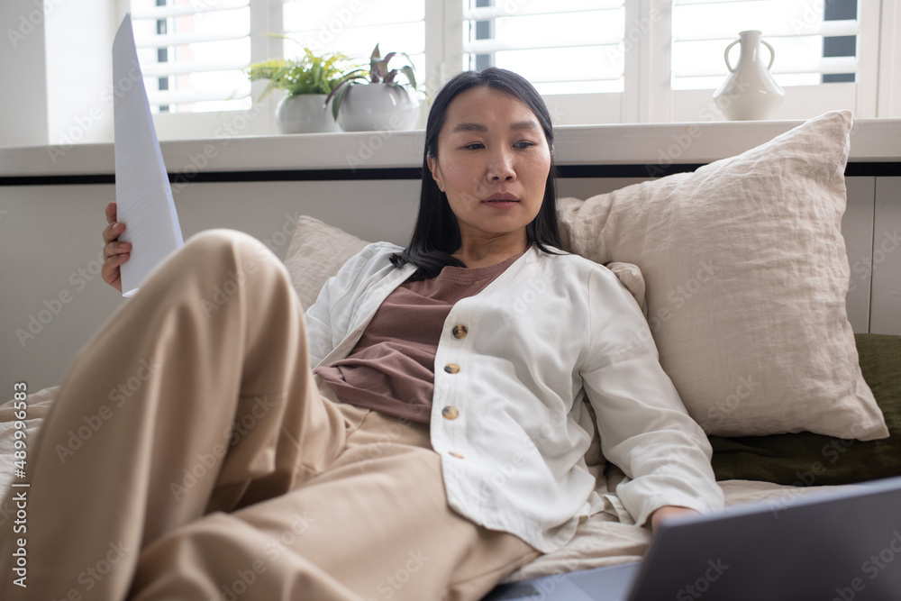 Poster serious female of asian ethnicity looking at data on laptop screen while searching for some particul