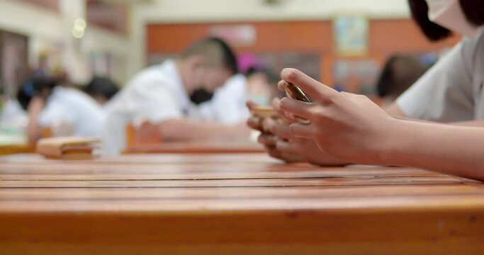Cut-in or b-roll shot of two students who are a lot of addicted to games. They are playing exciting games on  their mobile phones and sitting in the classroom.