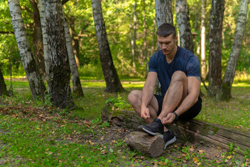 Man tying his shoelaces in the park outdoors, around the forest, oak trees green grass young enduring athletic athlete. active athlete nature, workout jogger fit person marathon, jogging Autumn