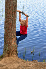 Middle aged woman in sportswear hanging on a stick with a rope above the water - 489999525