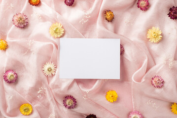 Fototapeta na wymiar Top view photo of the white card in the middle and many different colorful nice flowers scattered on the pastel pink textile background