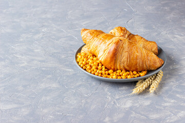 two croissants lie on a gray plate on a gray concrete background, minimalism of breakfast