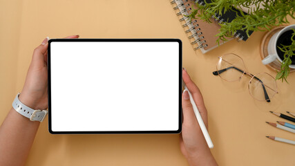 Female using stylus pen and digital tablet on beige background.