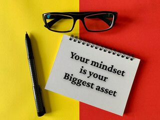 Motivational and inspirational concept - Your mindset is your biggest asset. With glasses, pen, yellow and red background. Motivational concept.