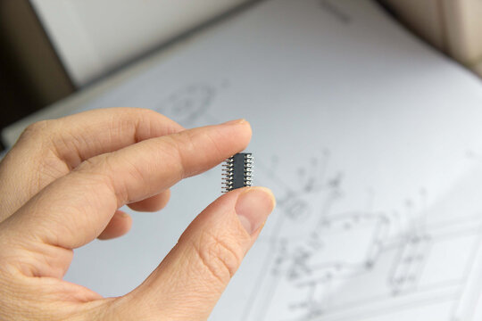 Hand holds chip compenent on drawings background. Engineering