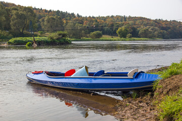 Fototapeta premium Kayak on the river bank. Blue canoe and scenic lake before the trip.