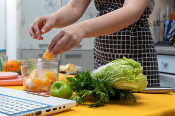The girl's hands put pieces of orange into the blender bowl. There are other ingredients and tools on the table for making fresh smoothie. Healthy eating. Selective focus.
