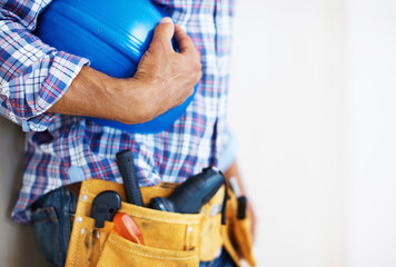 Fototapeta na wymiar Construction worker holding protective helmet. Mid section of construction worker with tool belt holding blue protective helmet.