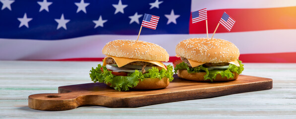 Top view closeup studio shot of two delicious tasty beef cheeseburgers with lettuce and tomatoes sliced placed on cutting board with United States of America national flag on old vintage wooden table