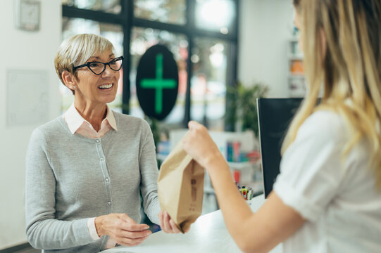 Happy senior woman customer buying medications at drugstore while talking with a female pharmacist