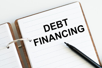 White notebook with the text DEBT FINANCING. Business concept