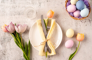 Table setting for Easter feast. Easter eggs, bunny, tulips and cutlery top view flat lay on...