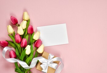 Bouquet of tulips, a gift box and a paper card on a pink background. Top view with place for text. Greeting on the occasion of Women's or Mother's Day.