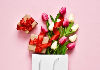 Flat lay composition with pink tulips and gift boxes in paper bag on pink background