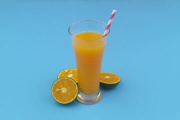 Orange juice glass with drink straw and orange fruits on blue background