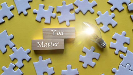 Obraz premium Top view of words - You matter with light bulb and jigsaw puzzle background.