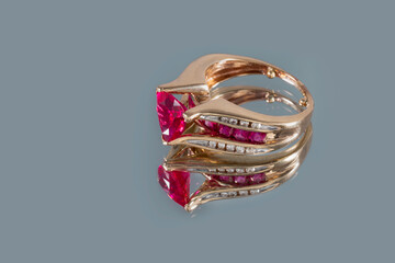 Beautiful yellow gold ring with ruby and diamonds on a gray mirror background with a close-up