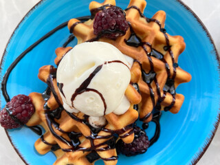 Belgian waffles with scoop of ice cream, fresh berries and chocolate topping on blue plate close up. Food background with selective focus